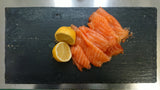 curls of wafer thin cold smoked salmon with half a lemon dressed on a slate
